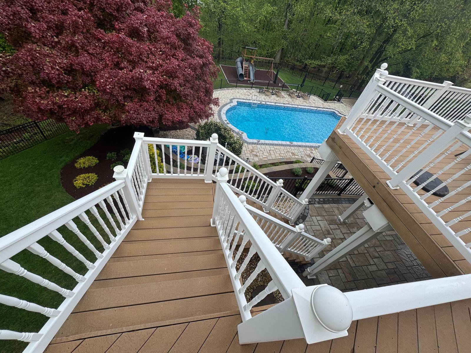 Completed multi-level deck with white railings and stairs leading to a pool area