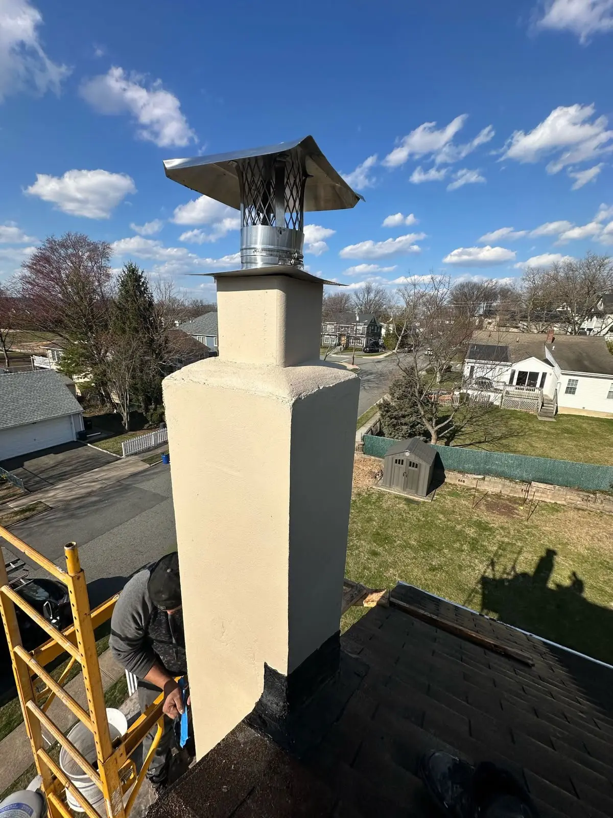 Chimney receiving a new stainless steel chimney cap while a worker seals the base