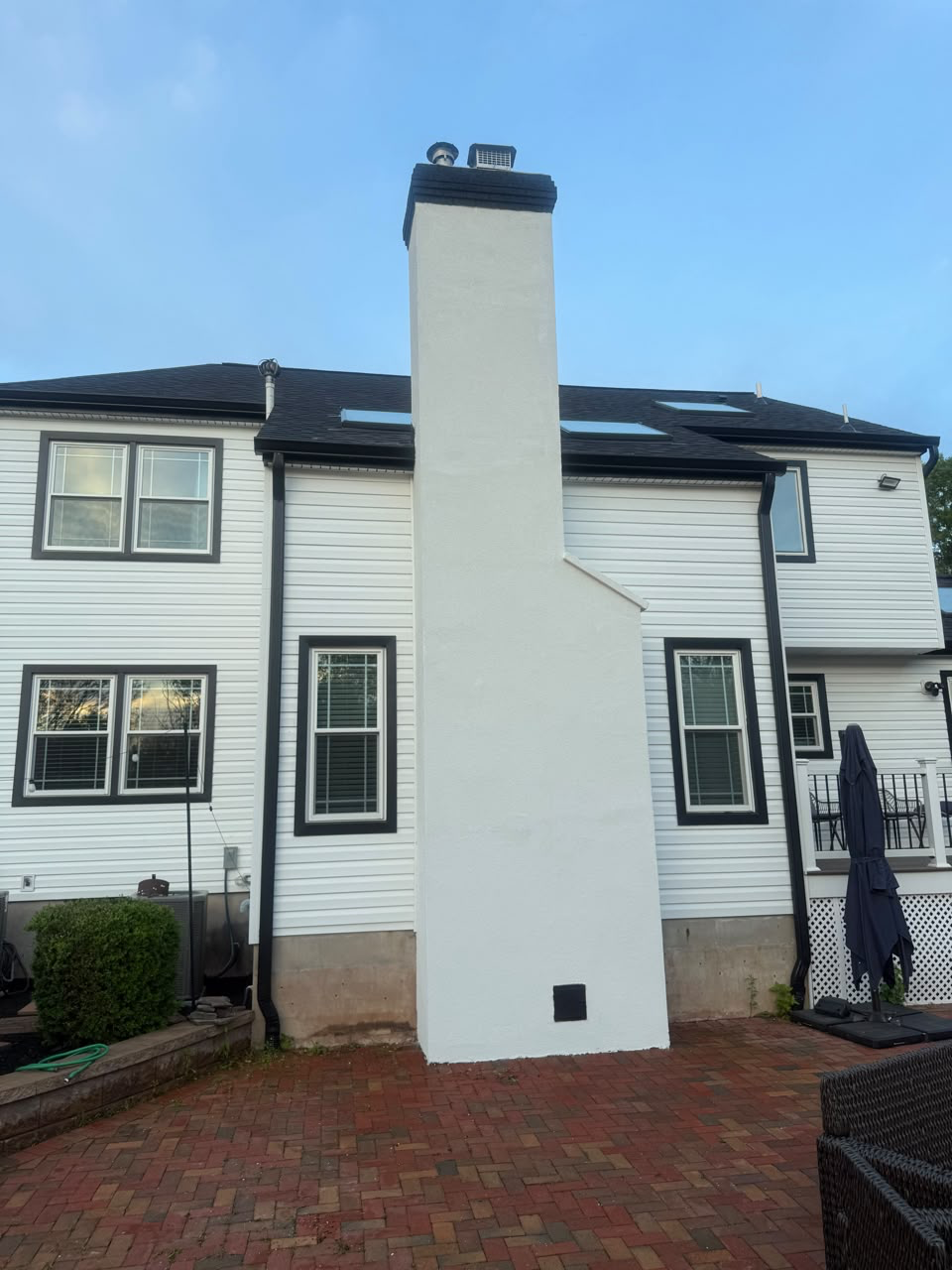 Tall white-painted chimney against a white-sided house with a dark shingle roof