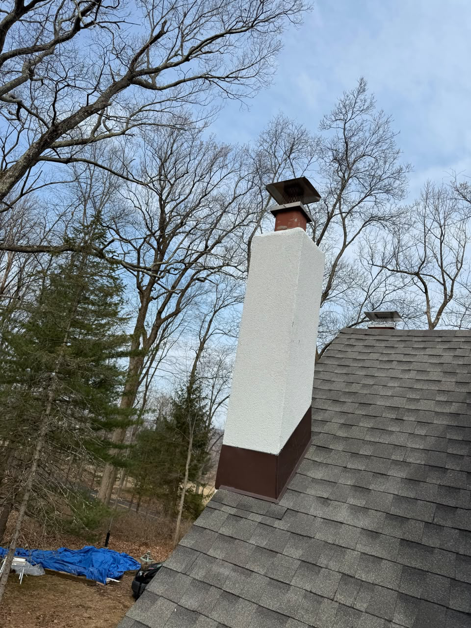Parged chimney with a new metal chimney cap and brown flashing on a grey shingle roof
